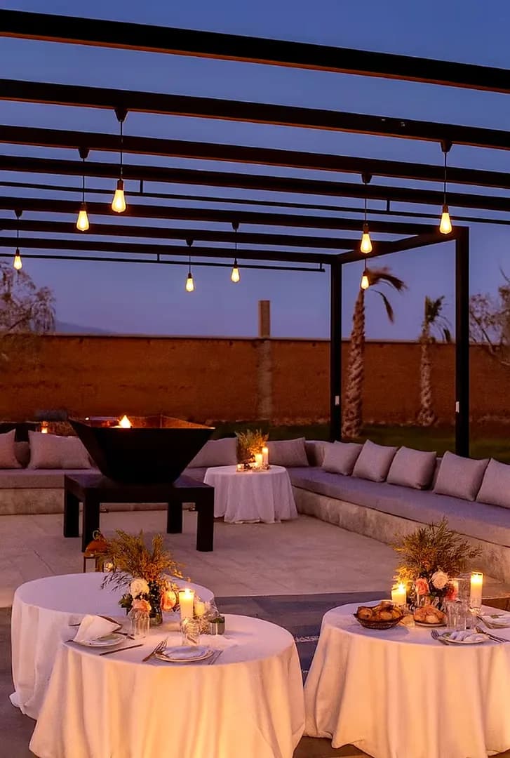 Tables rondes dressées aux bougies sous la pergola des Domaines du Sahara